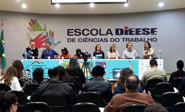 Foto muestra ocho panelistas. Detrás de ellos hay un banner que dice 