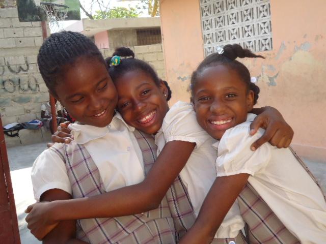 3 niñas haitianas con uniformes escolares abrazándose