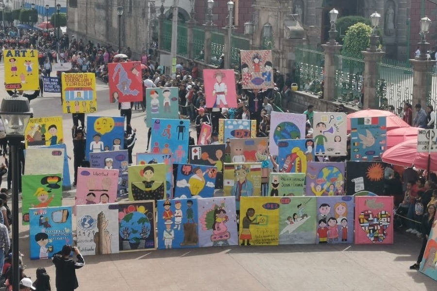 #ParaQueTodosVean La foto muestra una calle en México, hay un desfile de
pancartas realizadas por niños, niñas, jóvenes y adolescentes del país. Las pancartas tienen dibujos y mensajes relativos al derecho a la educación y a los derechos de los niños, niñas y adolescentes. A lado y lado de la calle hay espectadores aglomerados.
En el extremo inferior izquierdo de la foto se ve el logotipo de la CLADE, que es un círculo naranja, dentro del cual personas dibujadas en color blanco se dan las manos. En el extremo inferior derecho de la foto, están los créditosde la foto, con el texto: “Foto: CADEM”. Fin de la descripción.